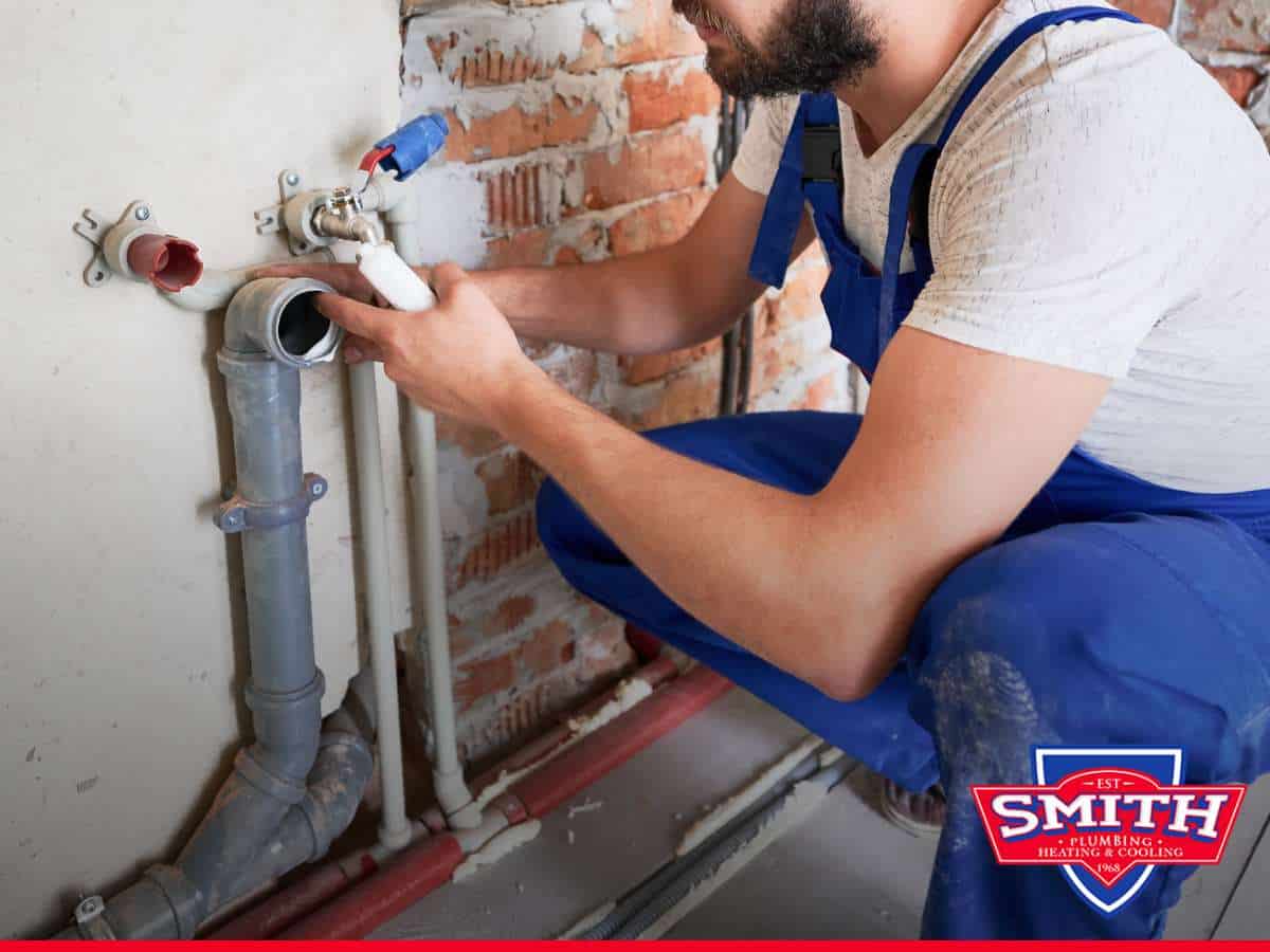 A plumber working on exposed pipes during a service call, emphasizing the need for regular plumbing maintenance