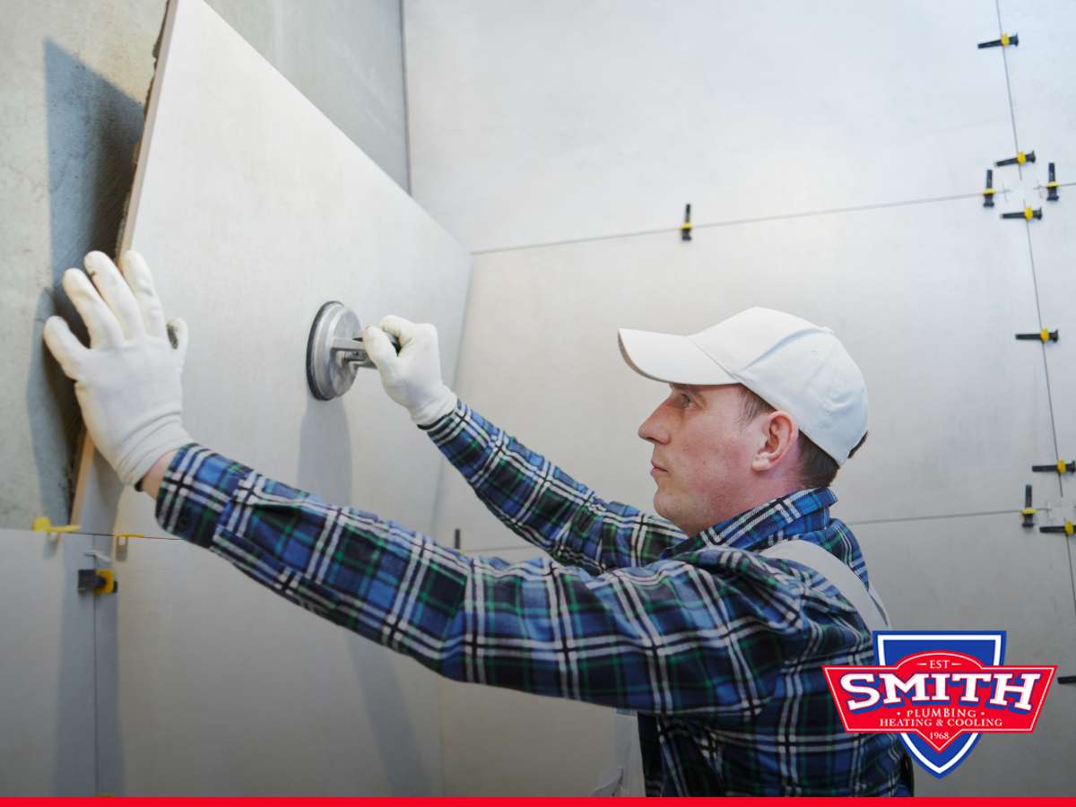 A plumber performs a bathroom makeover, carefully installing large tiles on the wall using spacers and a suction cup tool