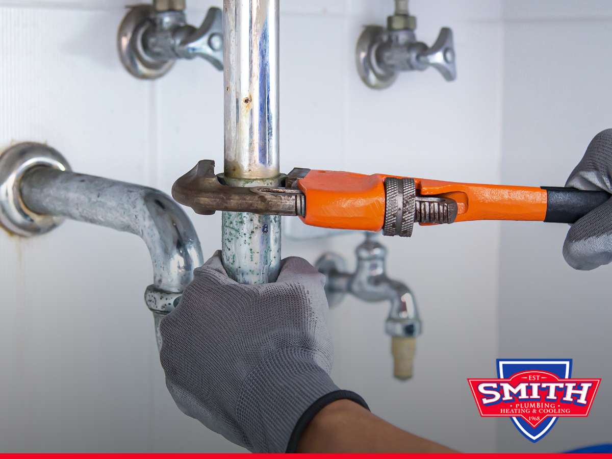 Plumber's hands using a wrench on pipes during a plumbing emergency.