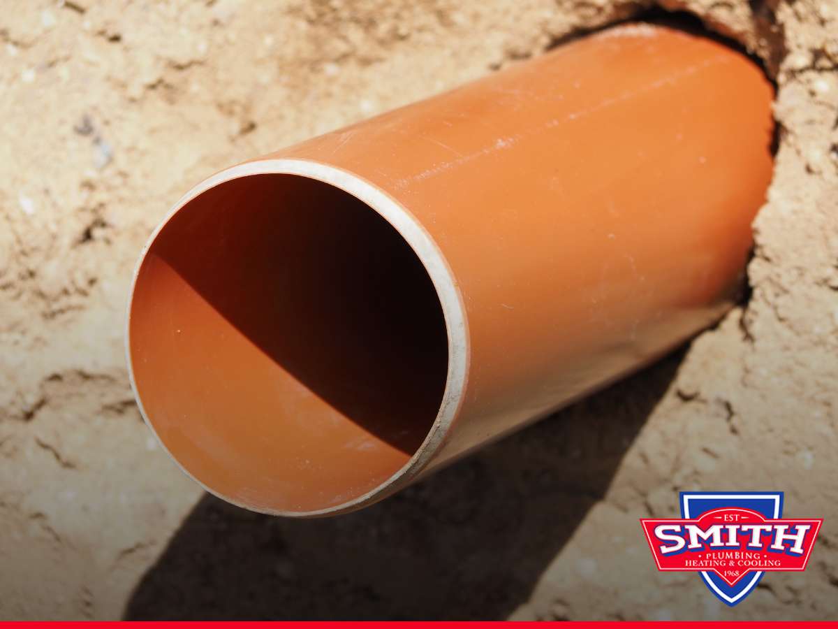 Close-up of an orange PVC pipe representing an old sewer line, with Smith Plumbing's logo on the right